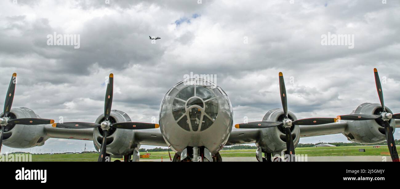 Front view of a World War II B-29 Super Fortress bomber with a commercial airliner taking off in the background in a dramatic sky. Stock Photo