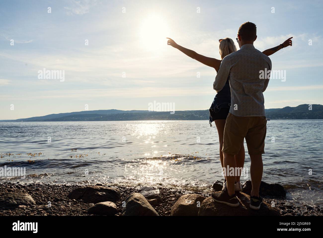 Man Standing Behind And Holding Girlfriend With Arms Outstretched Stock Photo