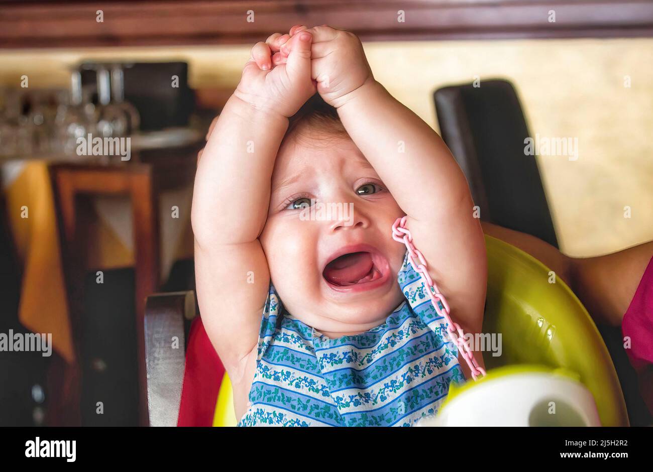 Young child throwing a tantrum in her high chair in a restaurant Stock Photo