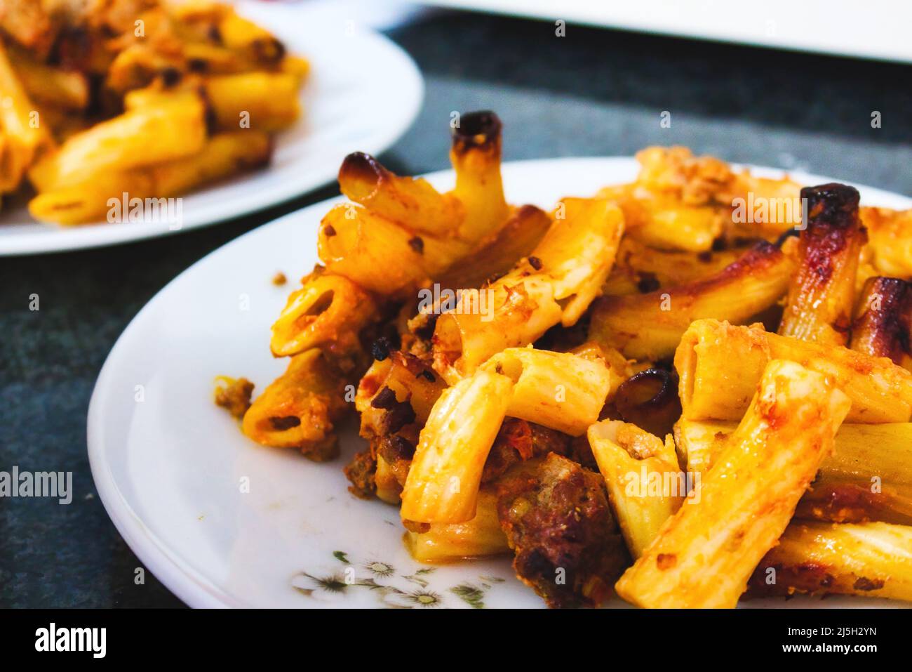 Penne pasta tubes with bolognese sauce on a white plate on a kitchen worktop Stock Photo