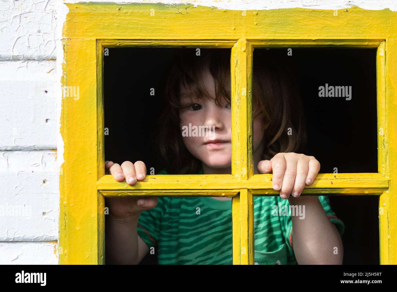 A little lad behind bars of a yellow window frame in an old playhouse Stock Photo