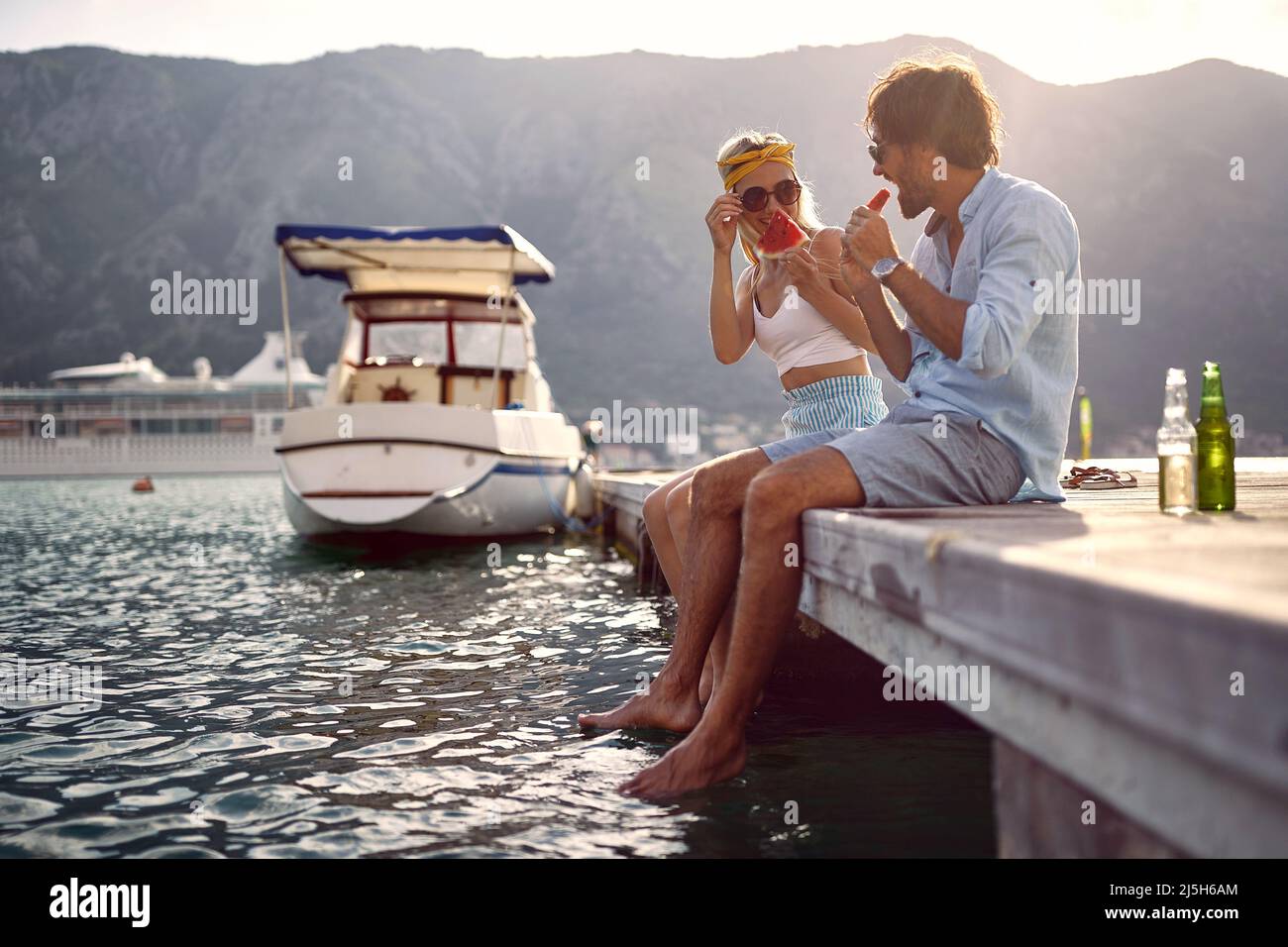 Loving smiling couple sitting on the pier on the lake, enjoying in the nature and eat watermelon Stock Photo