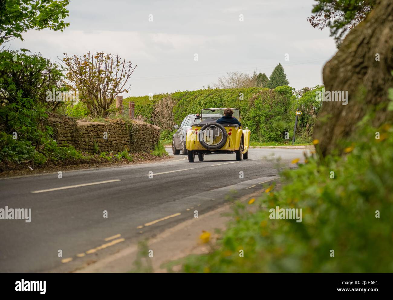 a yellow singer super 9 sports roadster automobile driving top down around a left hand bend on a country road Stock Photo