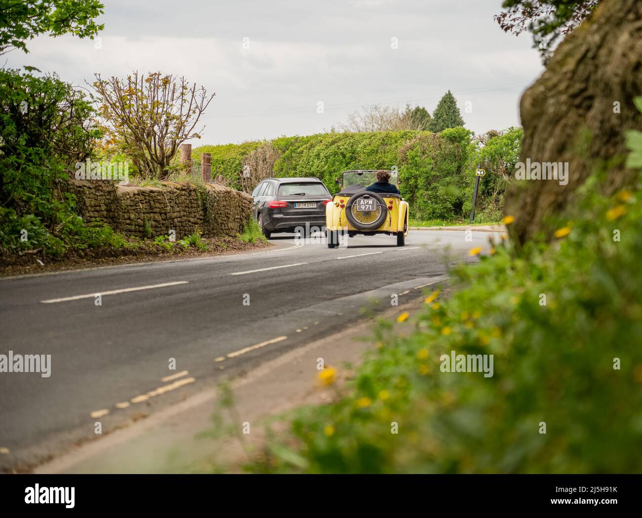a yellow singer super 9 sports roadster automobile driving top down around a left hand bend on a country road Stock Photo