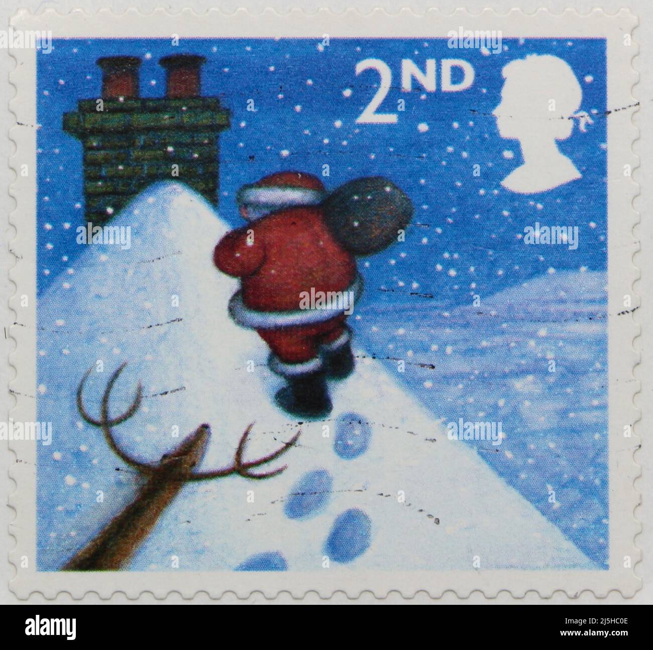 Photo of a British Christmas postage stamp with an illustration of Father Christmas on a snow covered rooftop walking towards a chimney 2004 Stock Photo