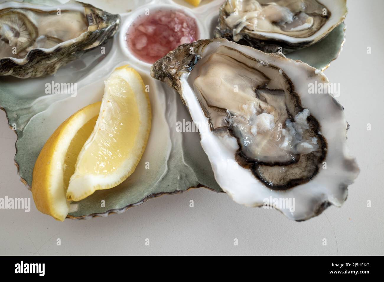 Selective focus view at fresh oysters with sliced of lemon on side, on white table. Stock Photo