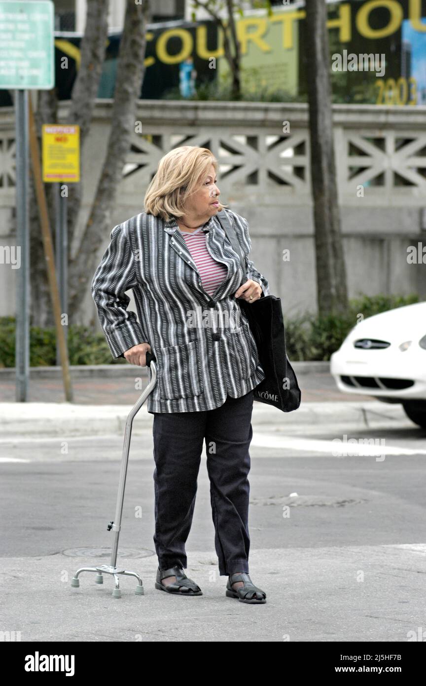 Senior woman with four footed cane crossing the street in traffic Stock