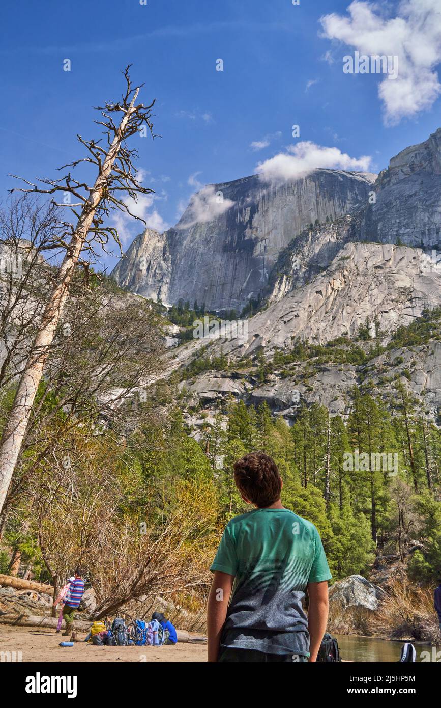A boy looking up at the enormous and steep Half Dome, Yosemite National Park, California; sunny spring day. Stock Photo