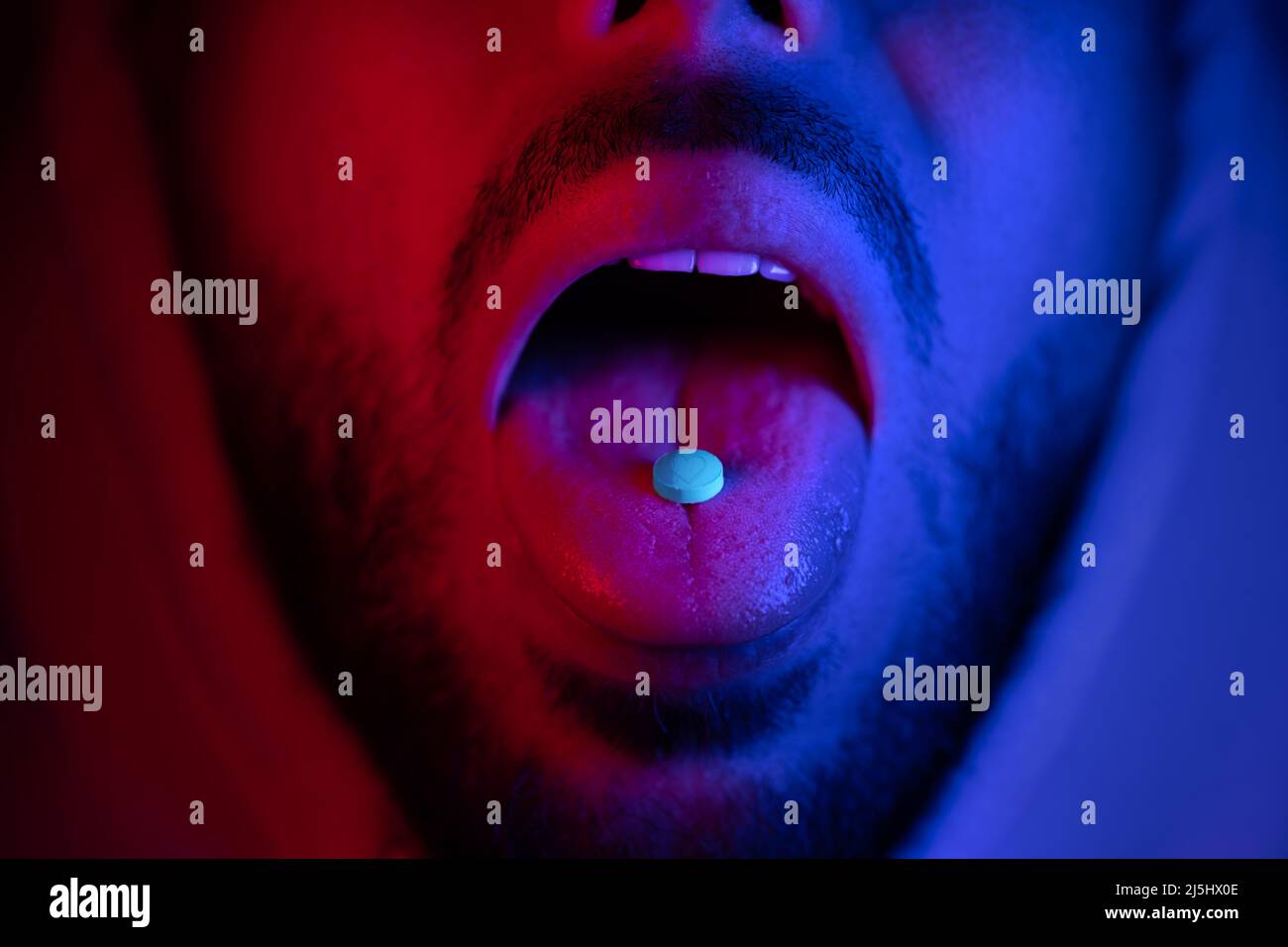 Close up of man mouth swallowing ecstasy drugs. Man taking MDMA ecstasy pill. Stock Photo