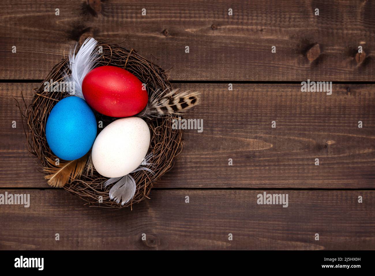 Multicolor decorated Easter eggs in the nest on a rustic wooden table. Easter concept. Stock Photo