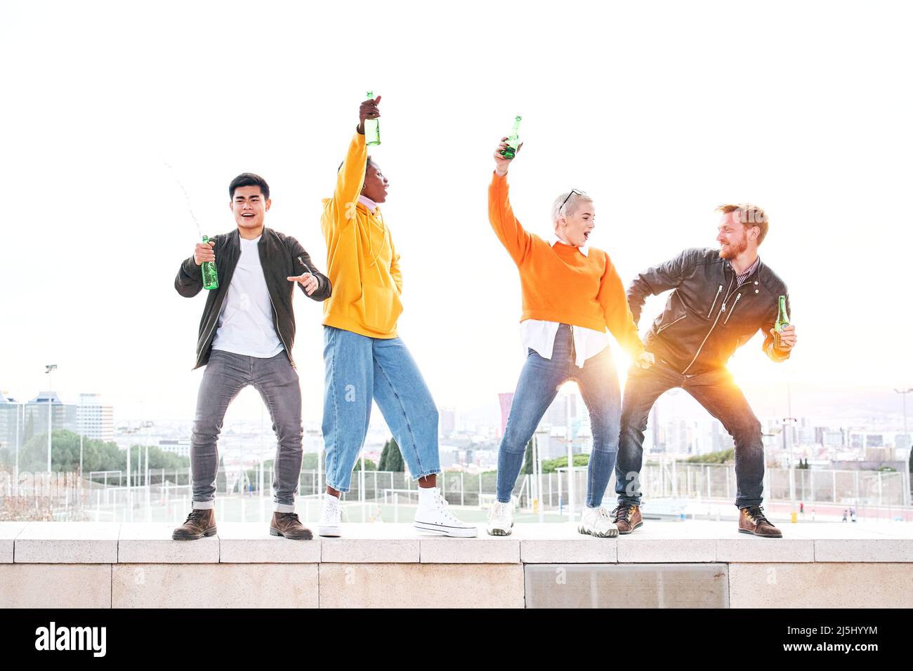 Group of diverse people dancing playfulness outdoors drinking beer and having fun. Happy friends celebrating together the success. Happiness and Stock Photo
