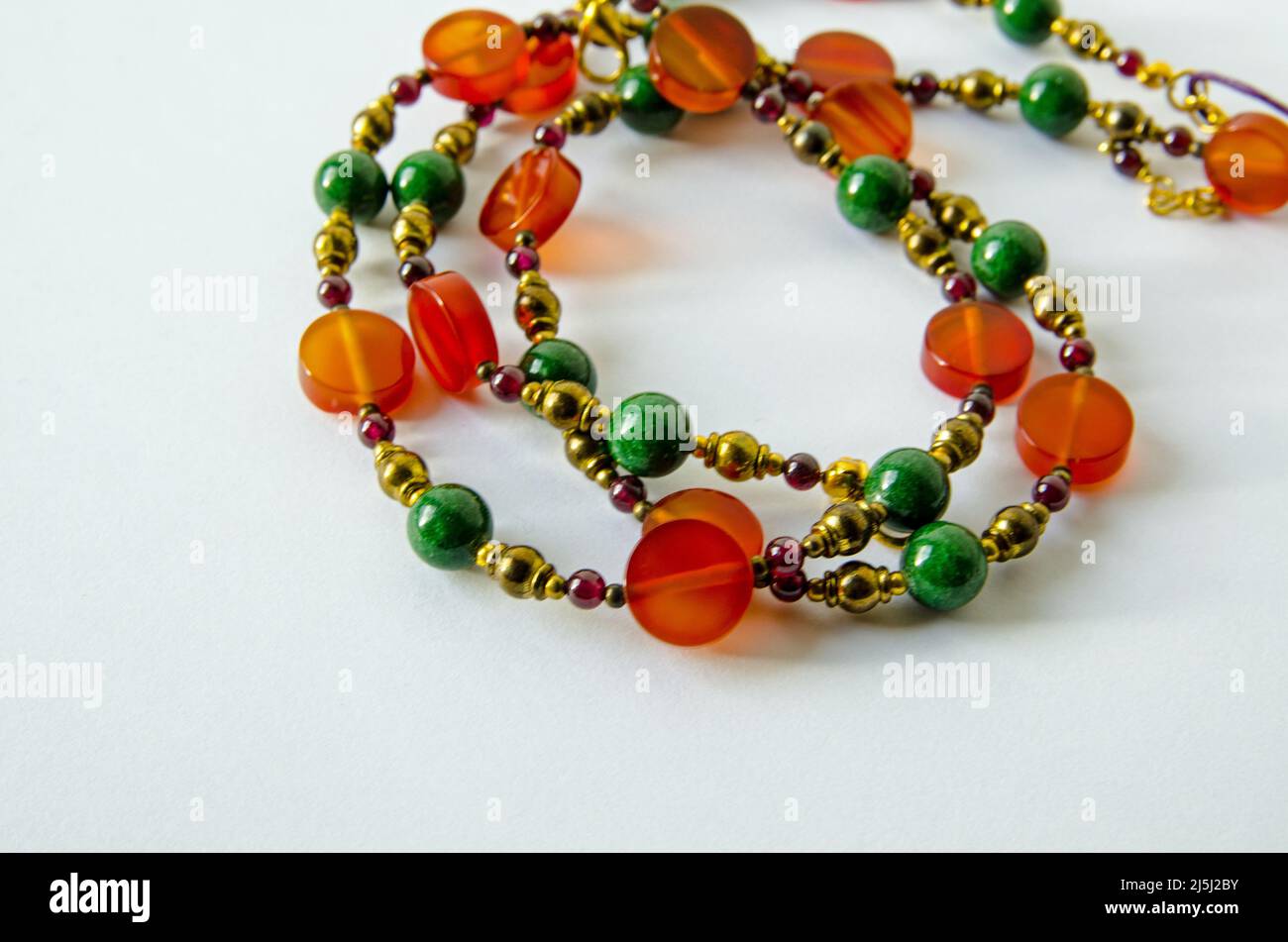 Handmade necklace crafted from beads of orange agate, red garnet and green quartzite intersperced with brass metal beads. Stock Photo