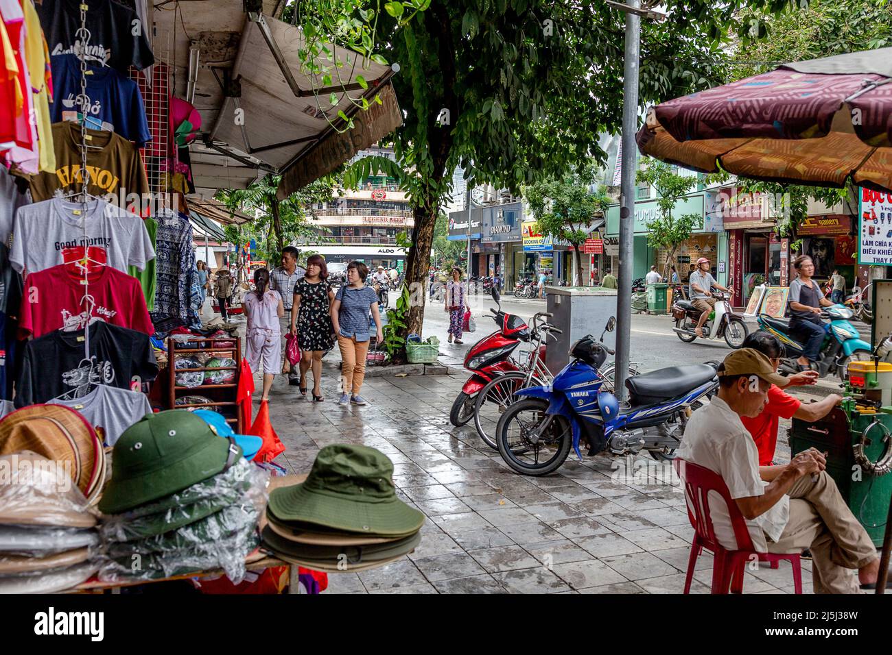 Shoppers in Hanoi walking on wet sidewalks while they shop in the clothing district of the Old Quarter. Stock Photo