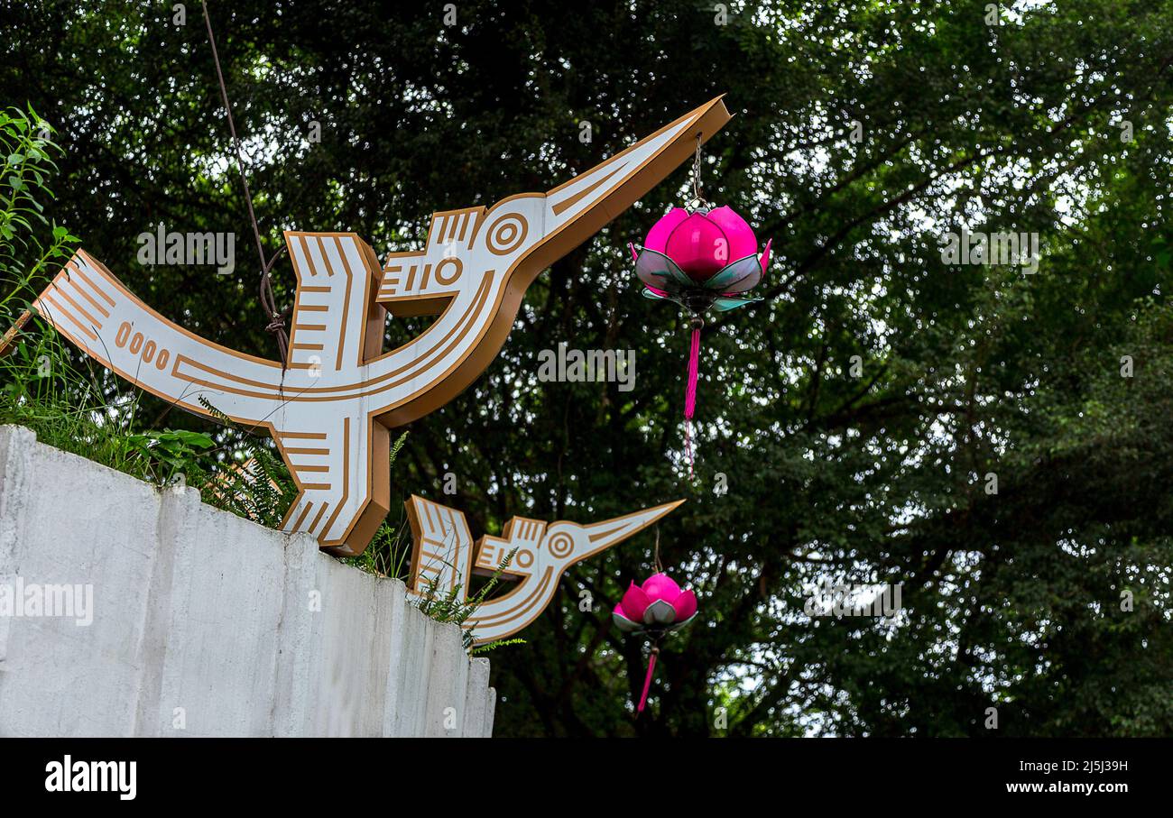 Two wood bird ornaments with hanging red ornamental flowers hanging under a tree in a lake park in Hanoi. Stock Photo