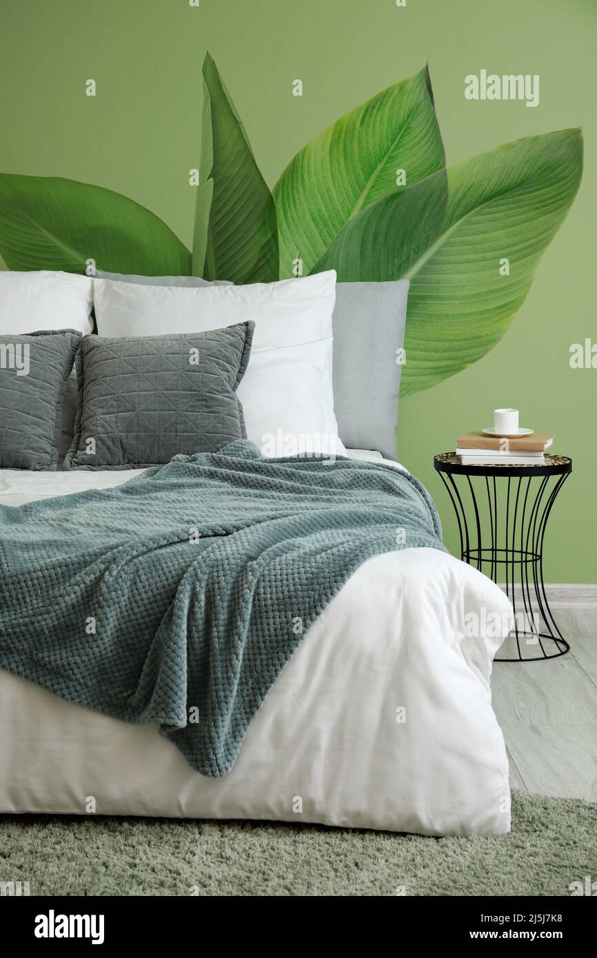 Big bed and small table near green wall with drawings of tropical