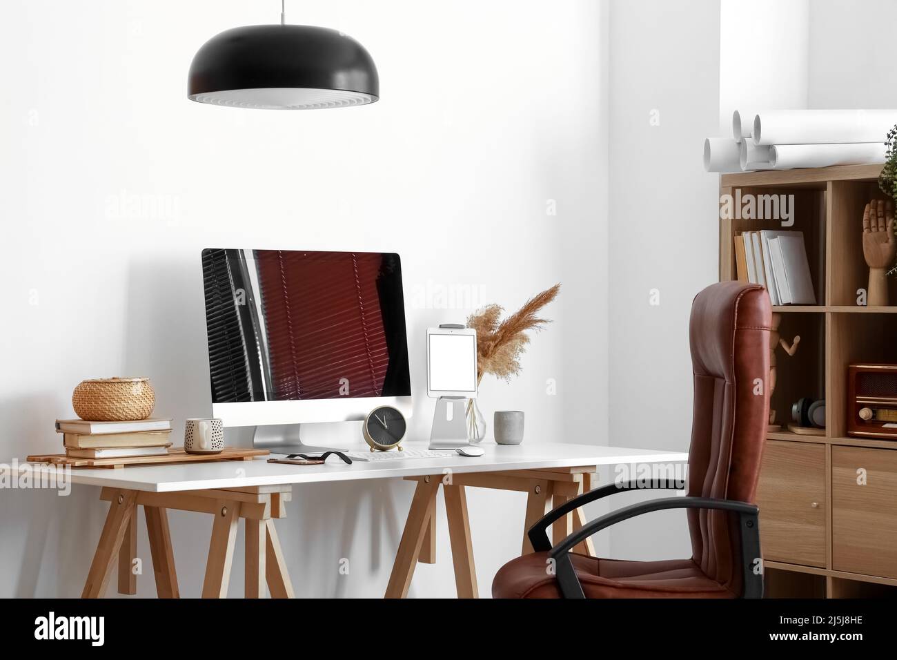 Modern computer, different gadgets, alarm clock and books on table near light wall Stock Photo