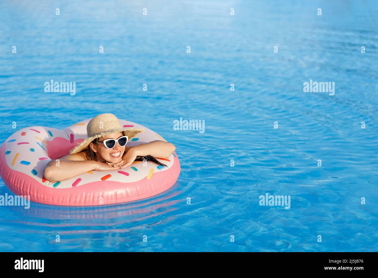 young woman in straw hat and sunglasses relaxing on inflatable ring in swimming pool Stock Photo
