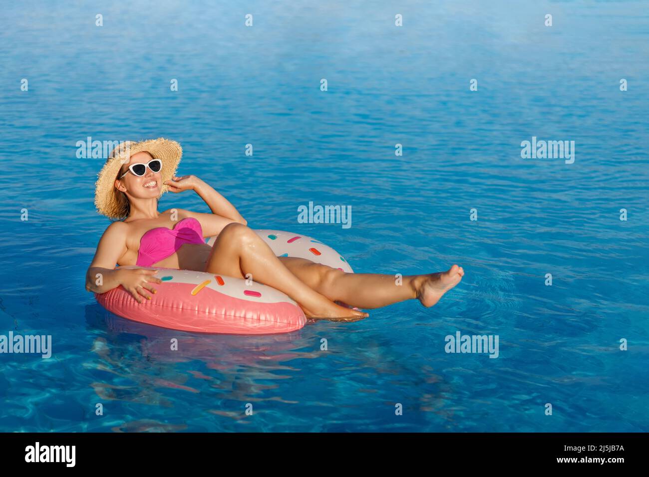 smiling young woman in straw hat and sunglasses relaxing on inflatable ring in swimming pool Stock Photo