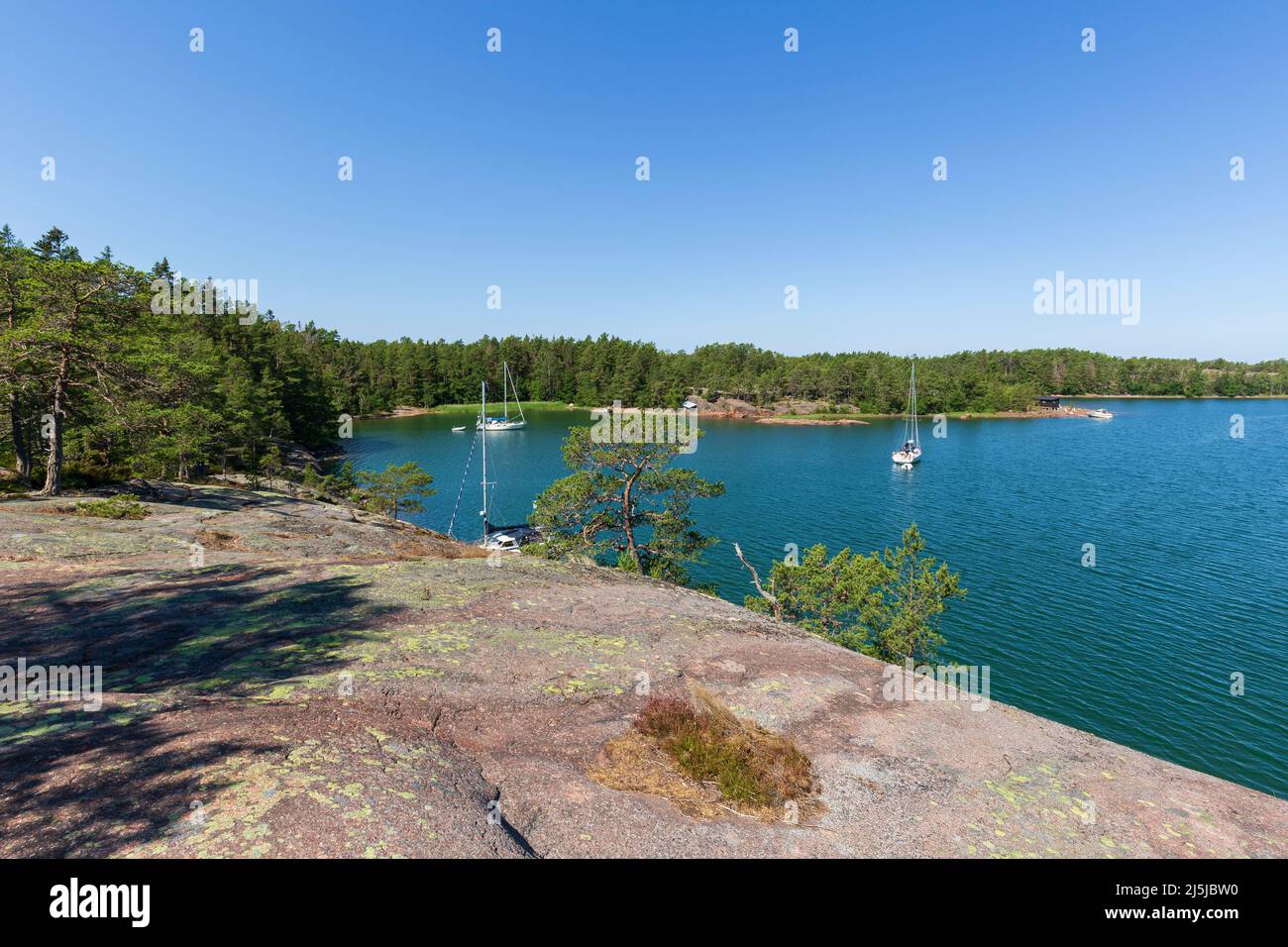 View of moored sailboats at sea and forested shoreline from a cliff along the Grottstigen cave nature trail at Geta in Åland Islands, Finland. Stock Photo