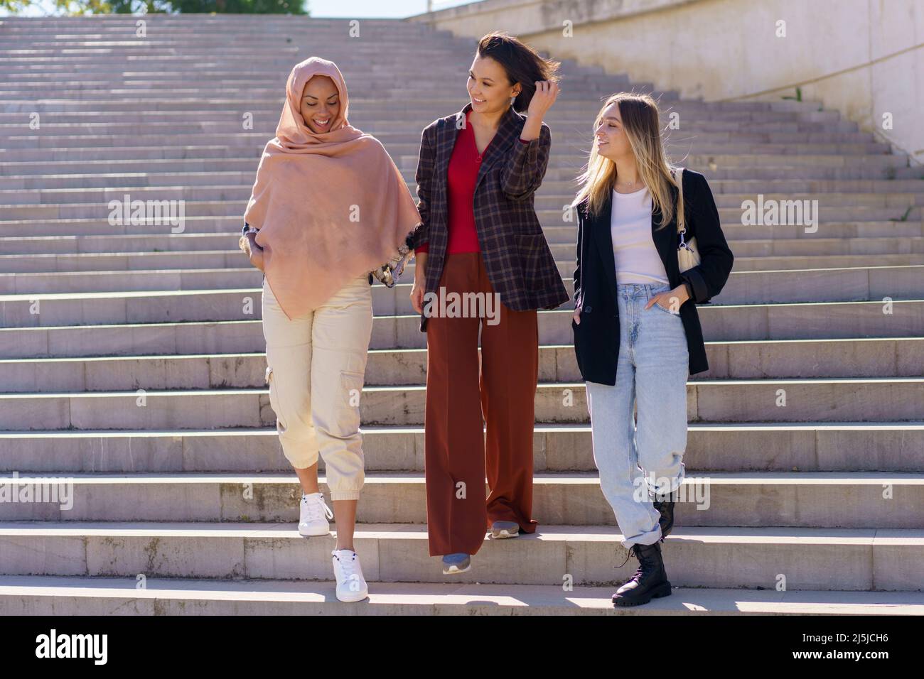 Positive young diverse women friends walking downstairs in campus Stock Photo
