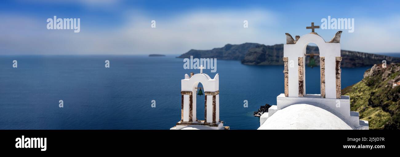 Santorini, Greece. Panorama of Greek Orthodox Church with two bell towers and blue calm sea in Oia village caldera, aerial view. Copy space, card temp Stock Photo