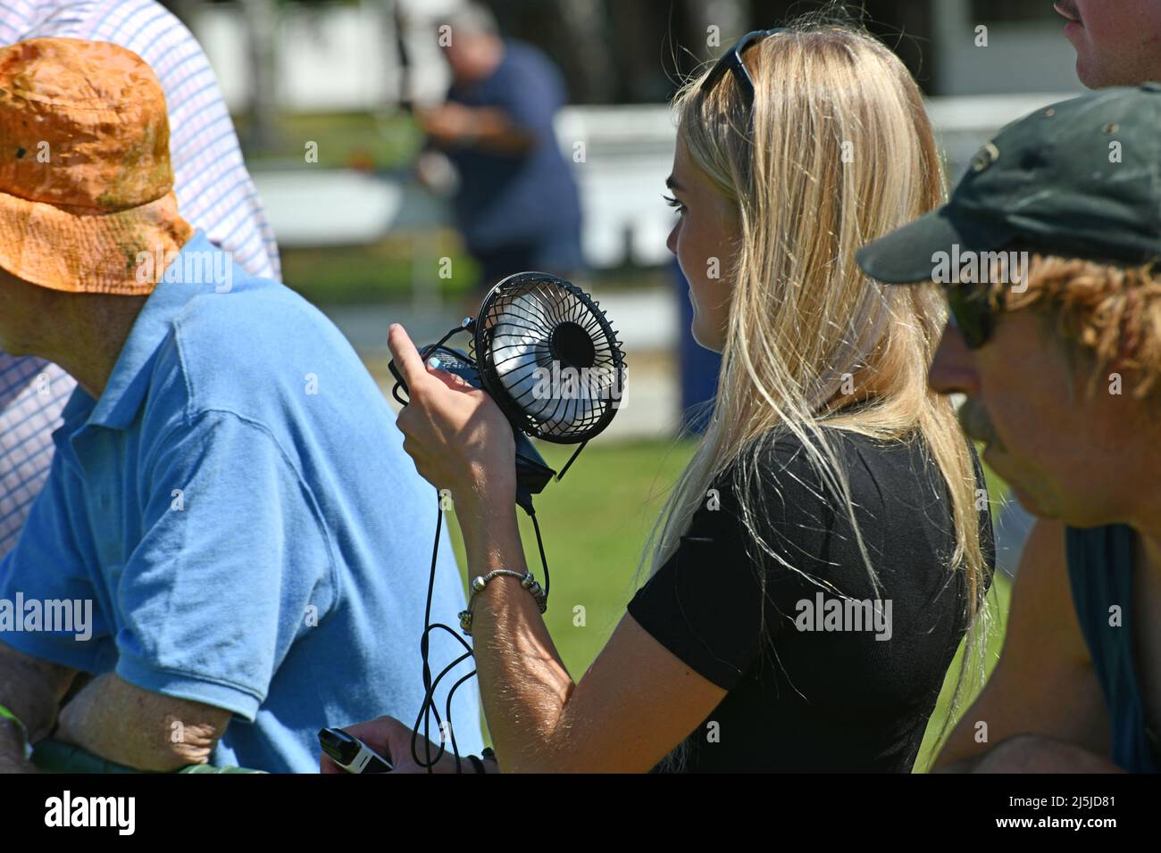 REEFTON, NEW ZEALAND, JANUARY 5 2022; A young woman uses a portable fan to keep cool at a country track meet, January 5, 2022 . Stock Photo