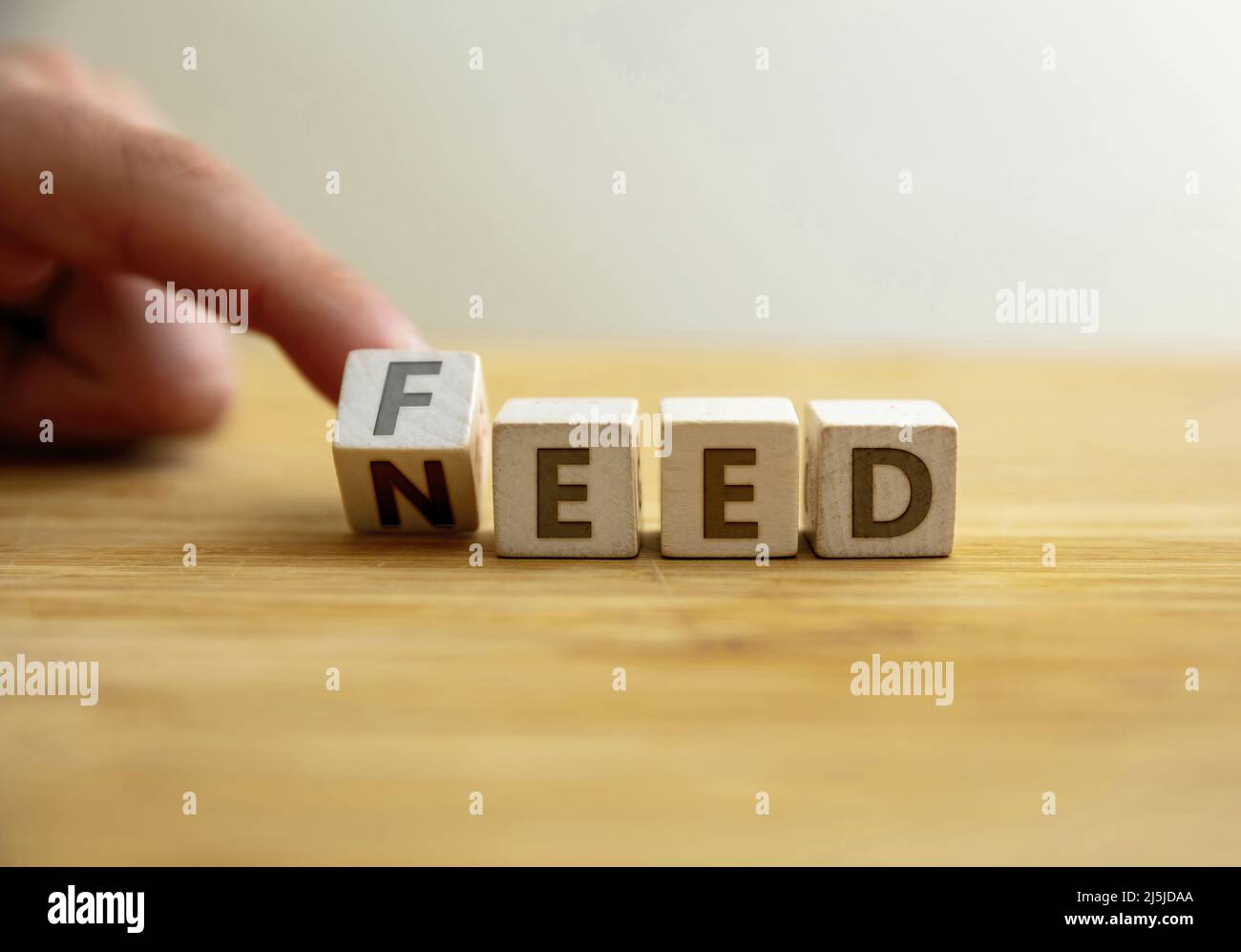 Need to feed concept. Hand flips letter on wooden cube changing the word need to feed. Message for food assistance, famine eradication, children malnu Stock Photo