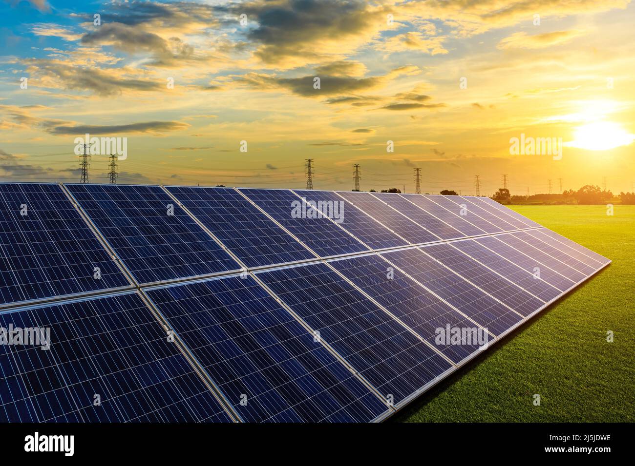 Solar panels and high voltage power tower with sky clouds at sunrise Stock Photo