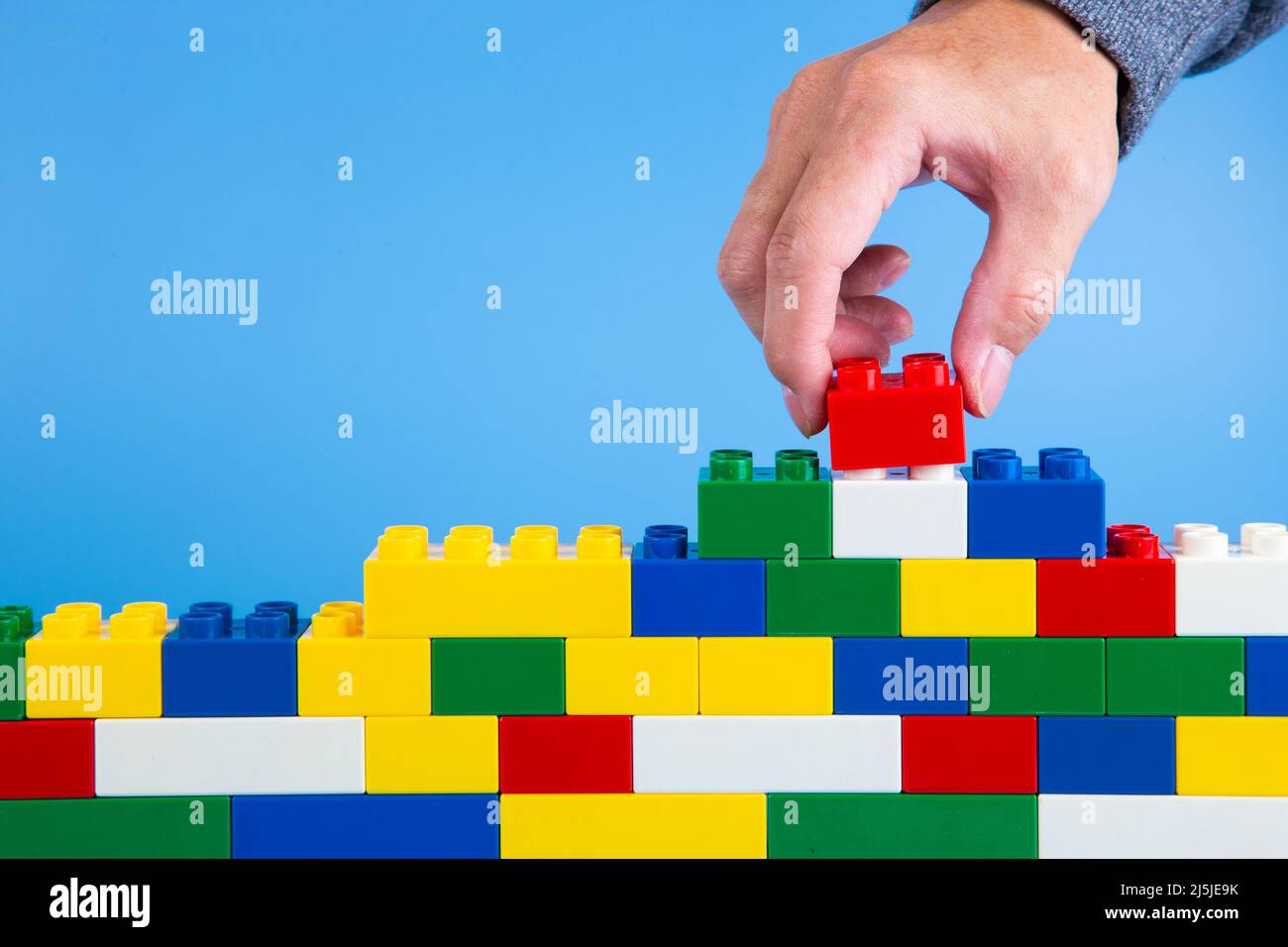 hand building up a wall by stacking up plastic block on blue background ...