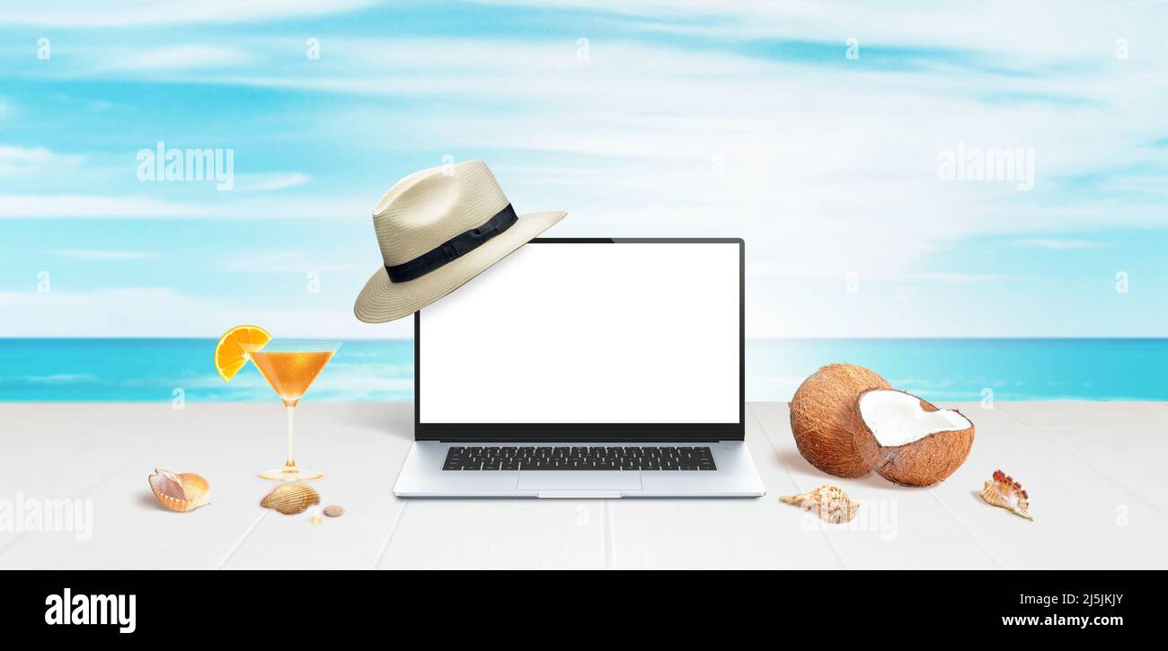 Laptop mockup with white hat on display on white surface with coconuts, shells and orange cocktail Stock Photo
