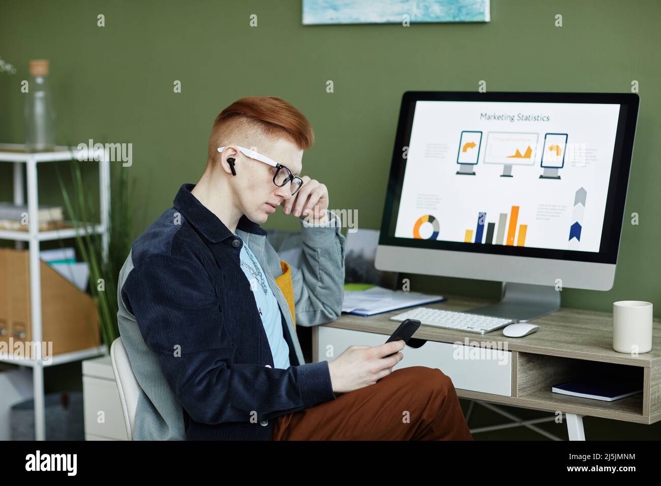 Side view portrait of trendy young businessman using smartphone while working at desk in green office Stock Photo