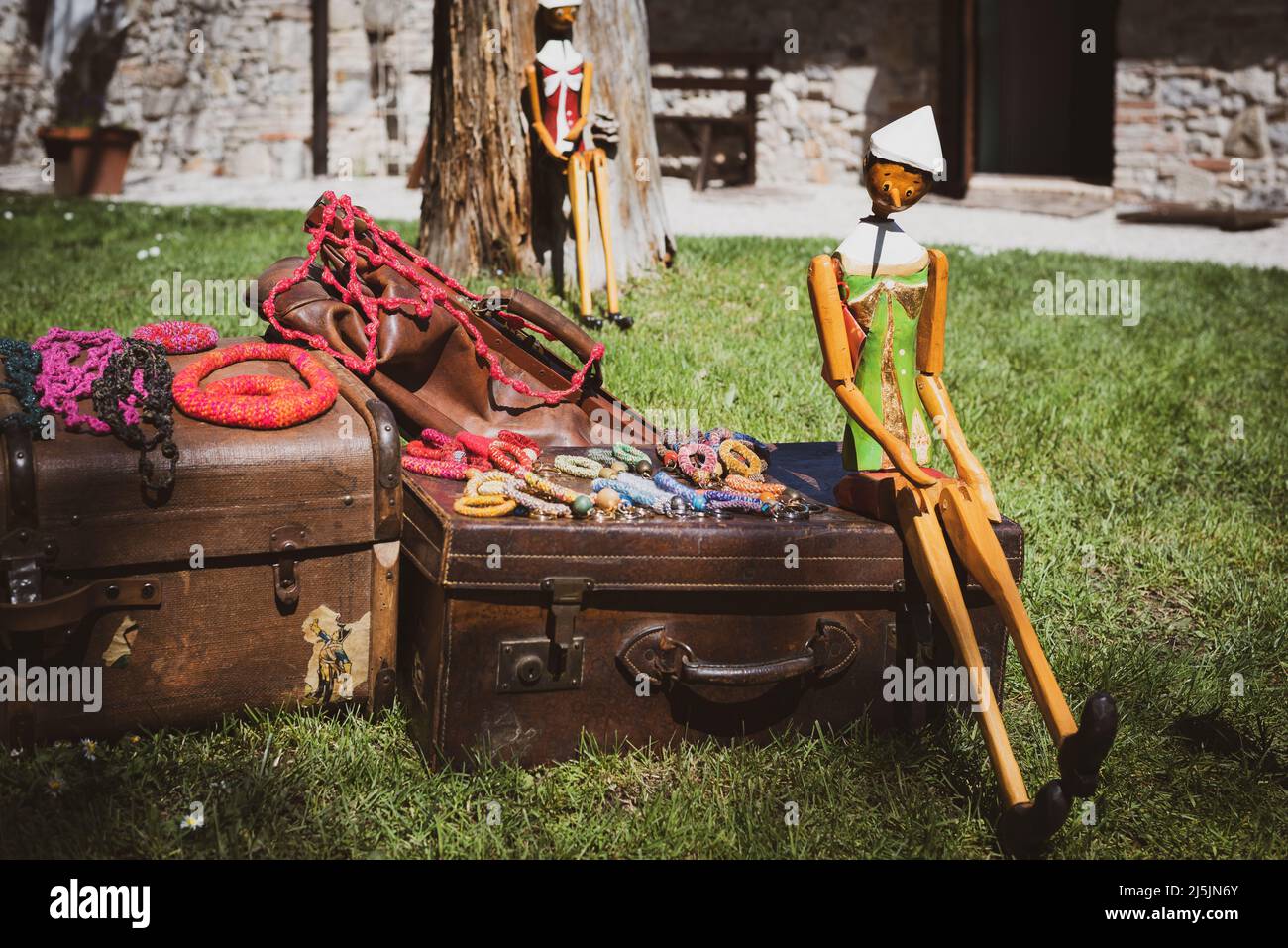 Pinocchio puppet sitting on a leather suitcase. Beautiful flea market on a garden. Stock Photo