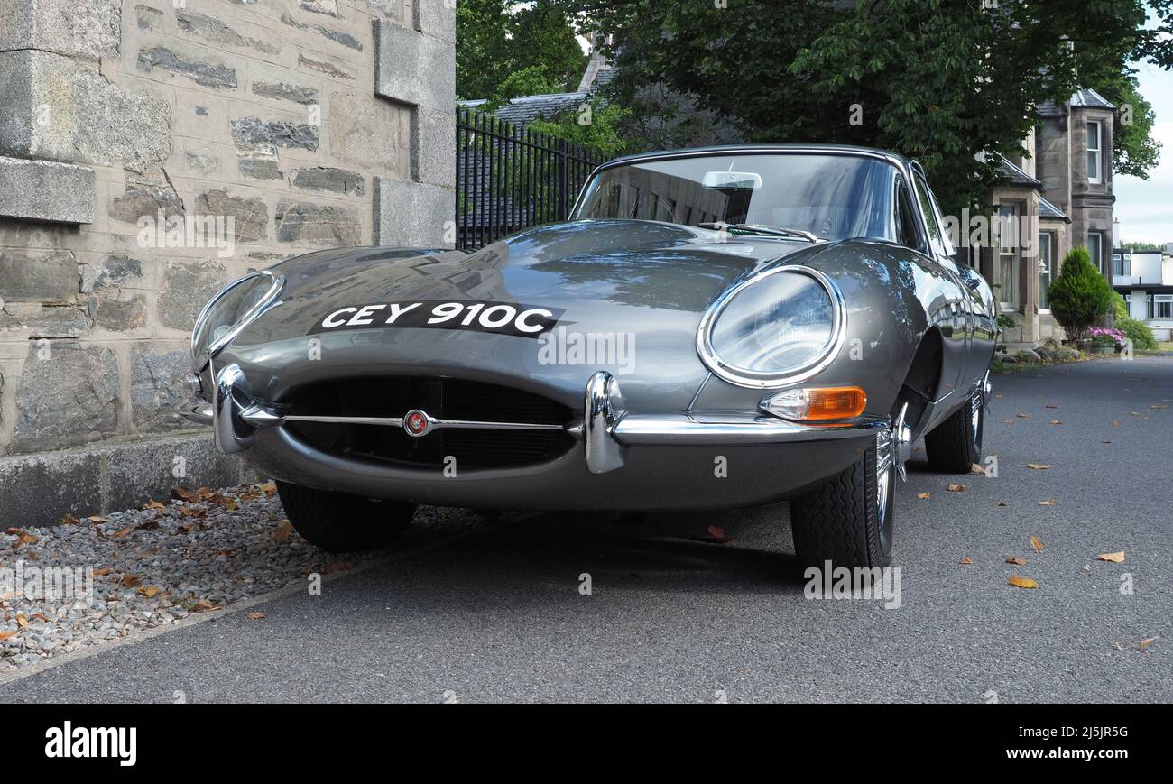 Front view of a Jaguar E-Type, Series 1 coupe, with a straight six 4.2lt engine, in metallic pearl grey silver. Parked in front of old stone building. Stock Photo