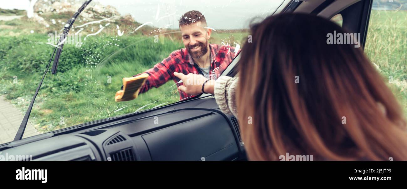 Man cleaning van windshield while woman pointing stain Stock Photo