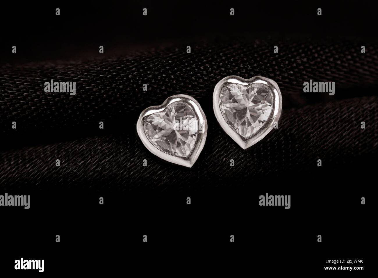Hearts-shaped silver stud earrings on black fabric background. Stock Photo