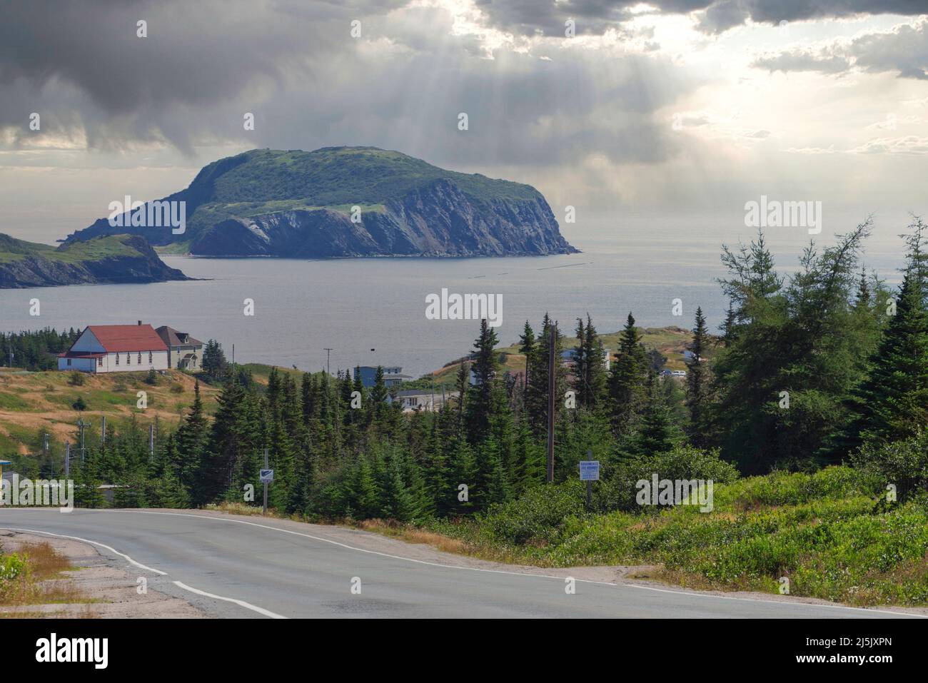 Road winding down to Tors Cove harbour with Fox Island on background, Newfoundland island, Canada Stock Photo