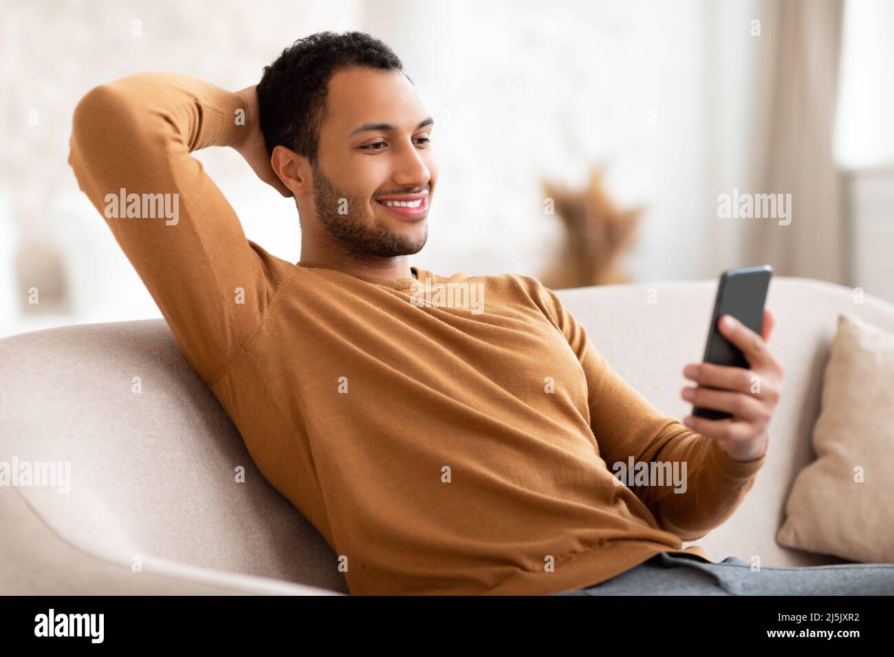 Portrait of smiling Arab man using smartphone at home Stock Photo