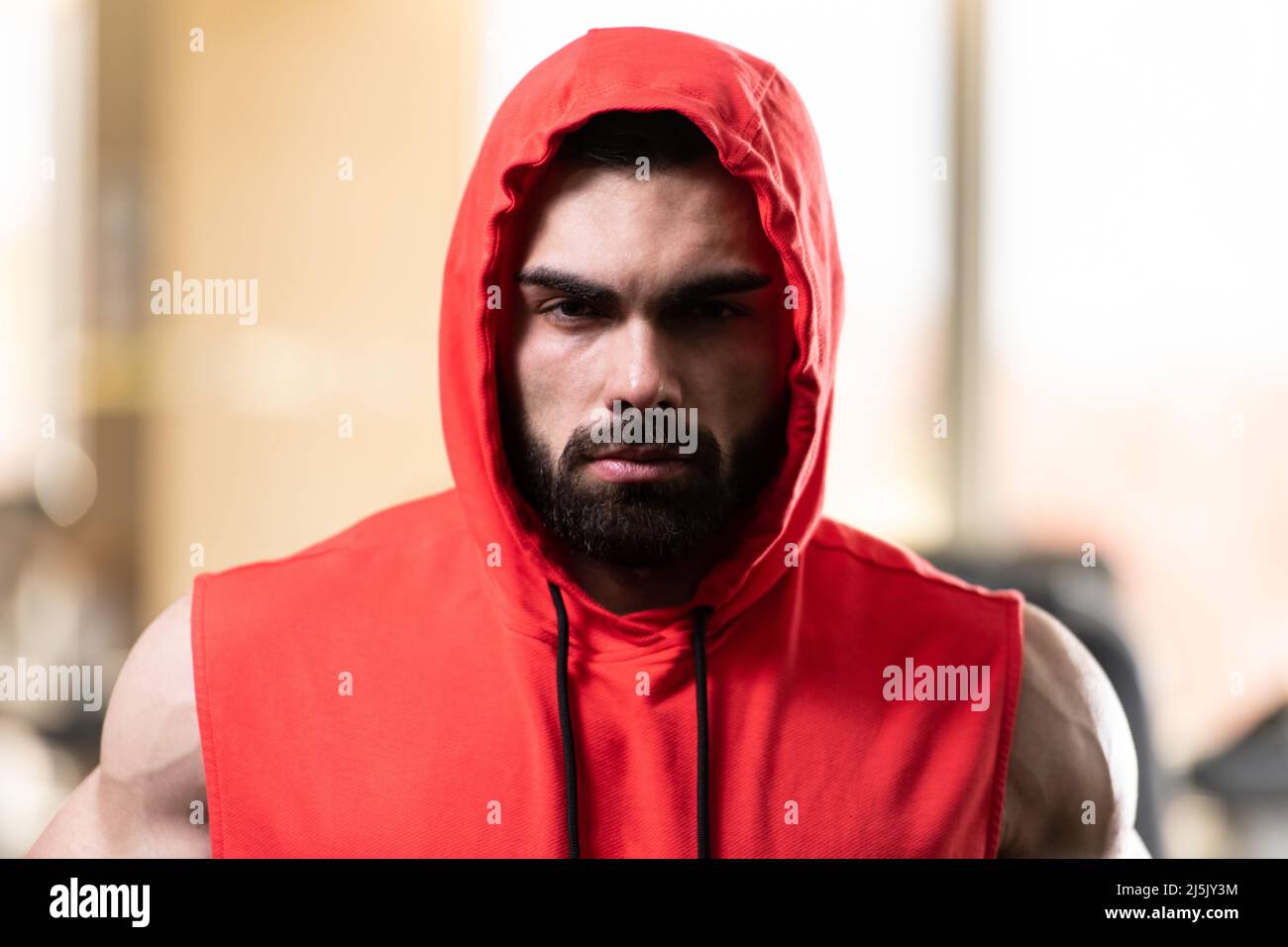 Healthy Young Man Standing Strong in the Gym and Flexing Muscles in a Red Hoodie - Muscular Athletic Bodybuilder Fitness Model Posing After Exercises Stock Photo