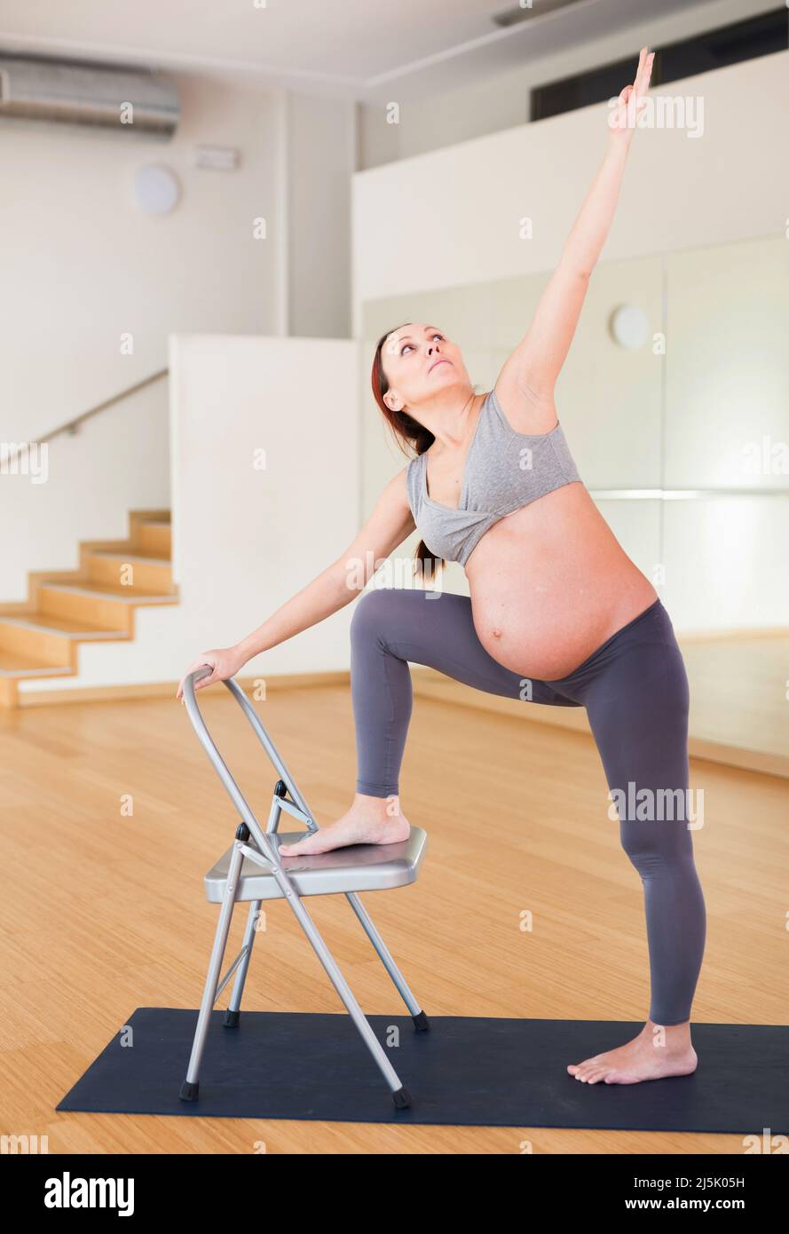 Pregnant woman is engaged in yoga. Chair Low Lunge Twist Pose or Parivrtta Sanchalasana Stock Photo