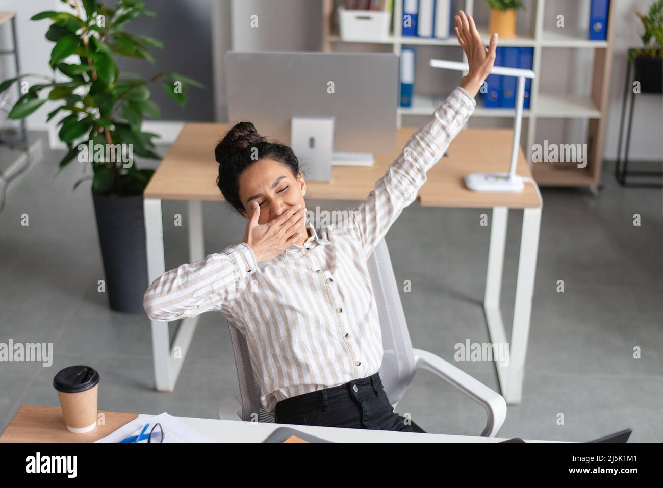 Sleepy young businesswoman yawning and stretching, tired of working in office, feeling sleepy at workplace, copy space Stock Photo