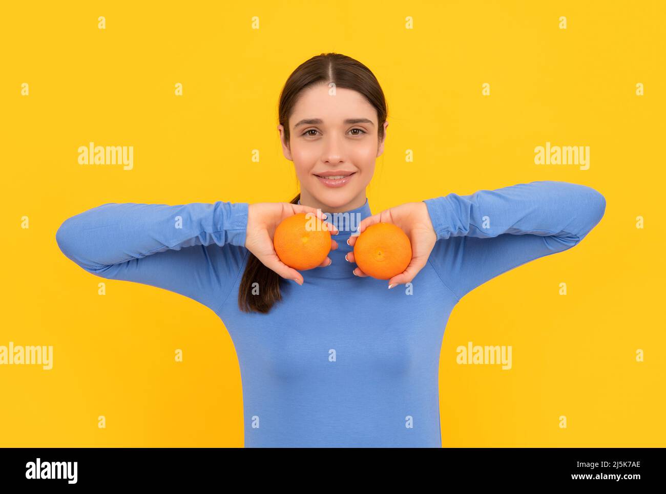 cheerful young woman holding orange citrus fruit on yellow background, skincare Stock Photo