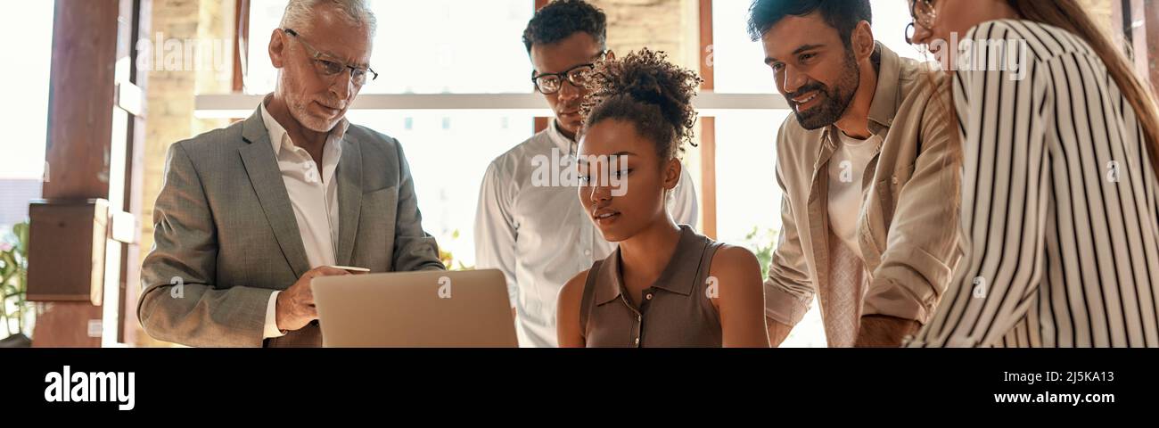 Successful team. Multicultural team looking at the laptop and discussing something while working together in the modern office Stock Photo