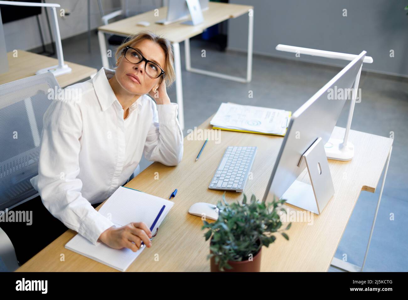 Tired business woman in white shirt and eyeglasses sitting at her desk ...
