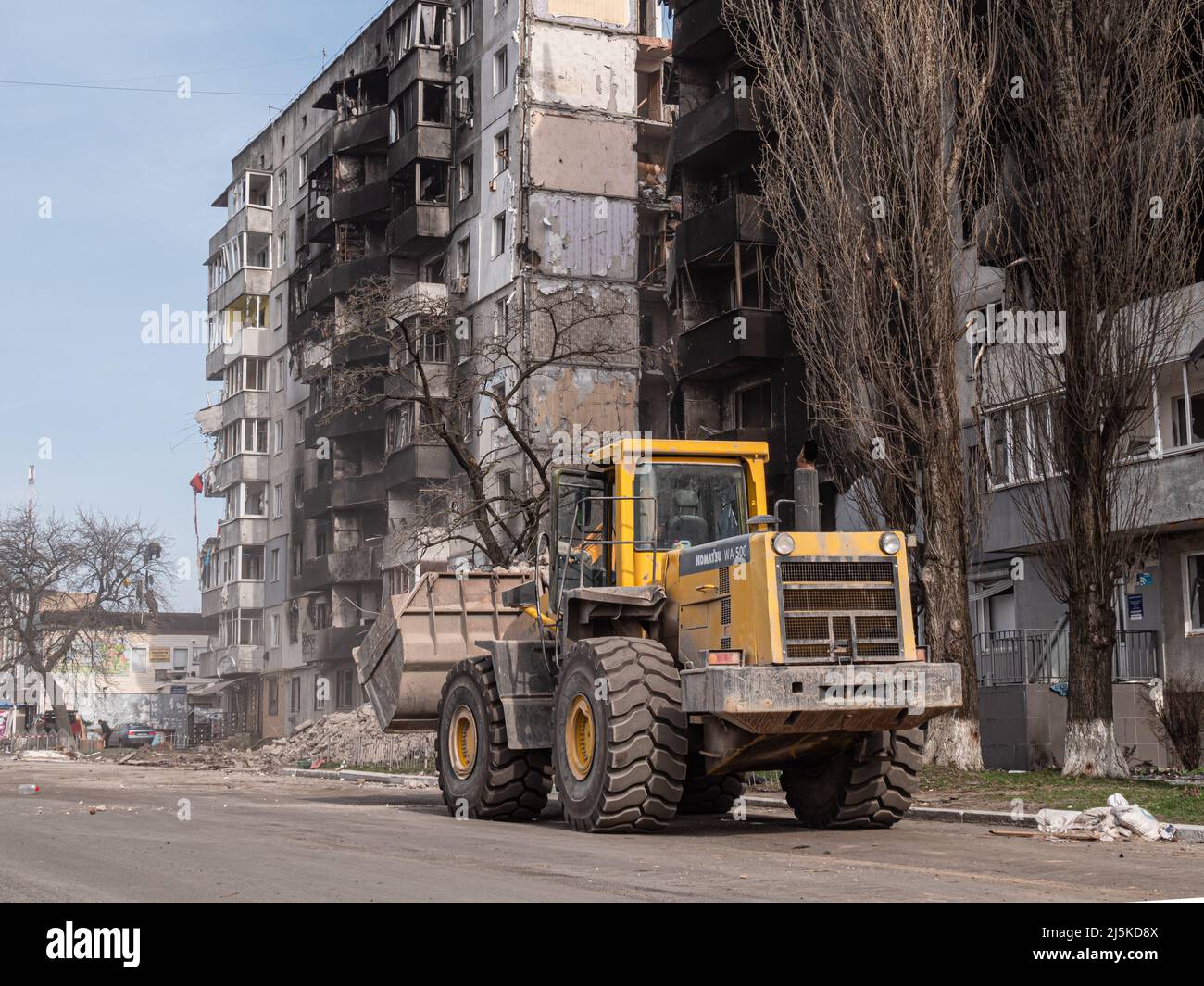 Borodyanka, Ukraine - April 2022: Excavator loads construction waste into truck for removal from site of explosion and destruction of building. Destroyed houses after rocket and air strikes. Stock Photo