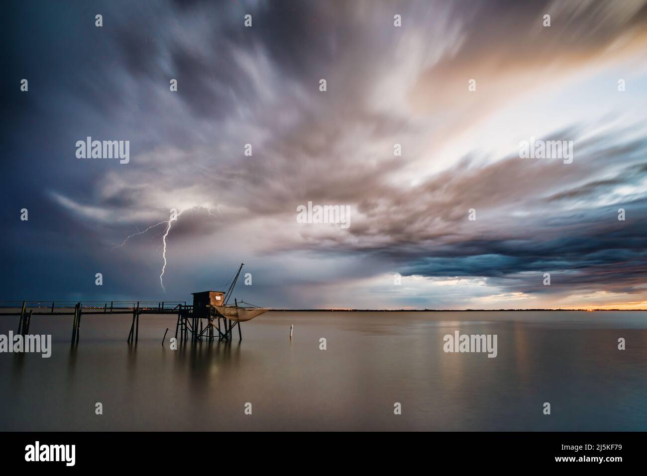 Dramatic storm clouds and calm sea at sunset west Atlantic coast France Gironde estuary, Charente Maritime with lightning strike on ocean horizon Stock Photo