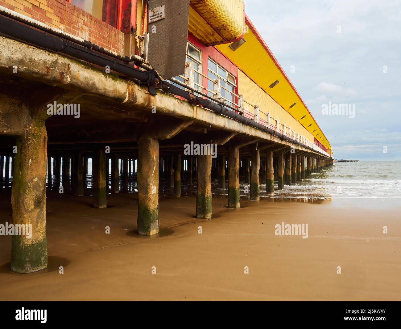 A fun fair complex on a pier, extending out into the sea at Frinton. The exposed, sea weed covered stanchions and cracking paint give a desolate feel. Stock Photo