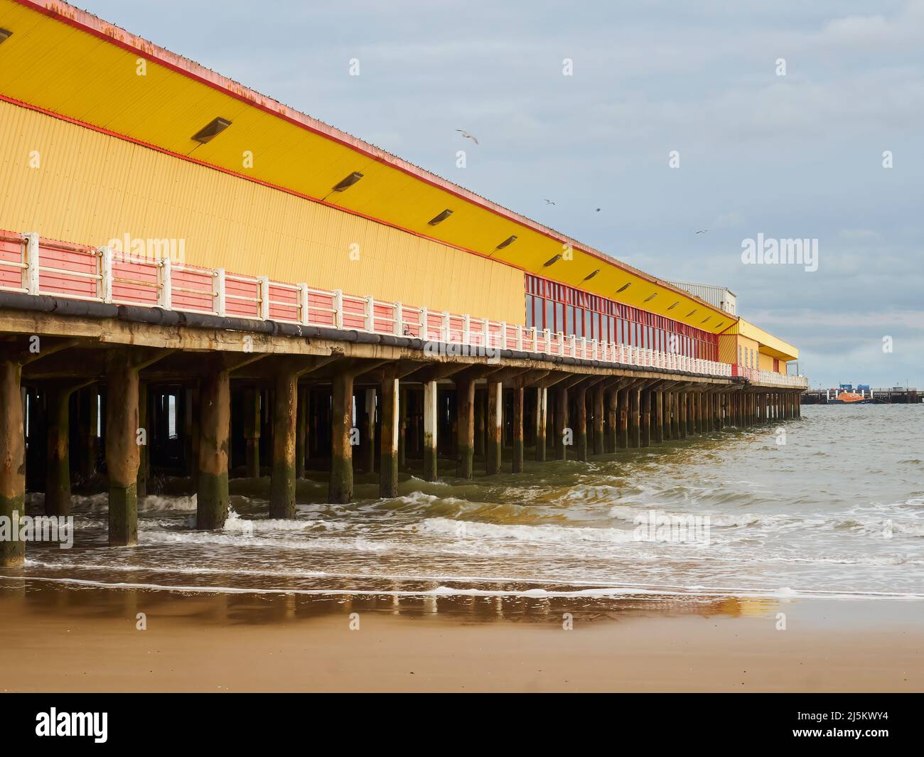 A fun fair complex on a pier, extending out into the sea at Frinton. The exposed, sea weed covered stanchions and cracking paint give a desolate feel. Stock Photo