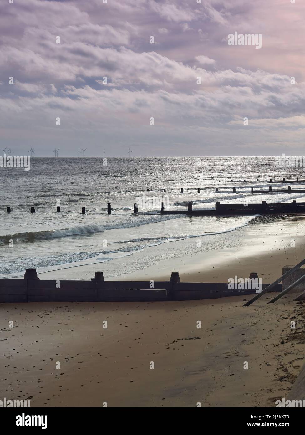 Waves breaking on Frinton Beach, with sunlight breaking through storm clouds overhead to reflect in soft, glowing light from the shimmering sand. Stock Photo