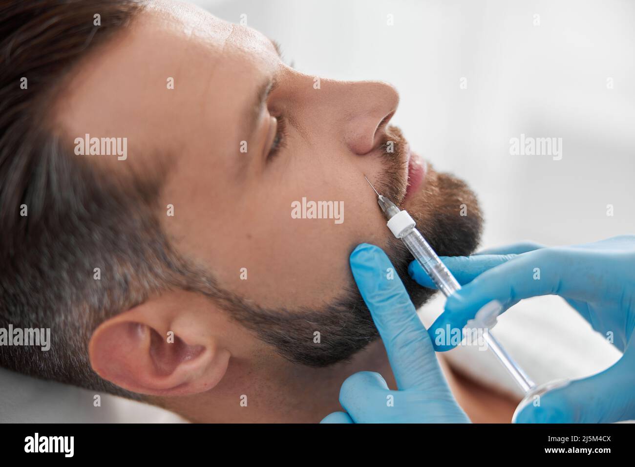Mature person with beard undergoes nasolabial fold filler procedure with skilled beautician in salon Stock Photo