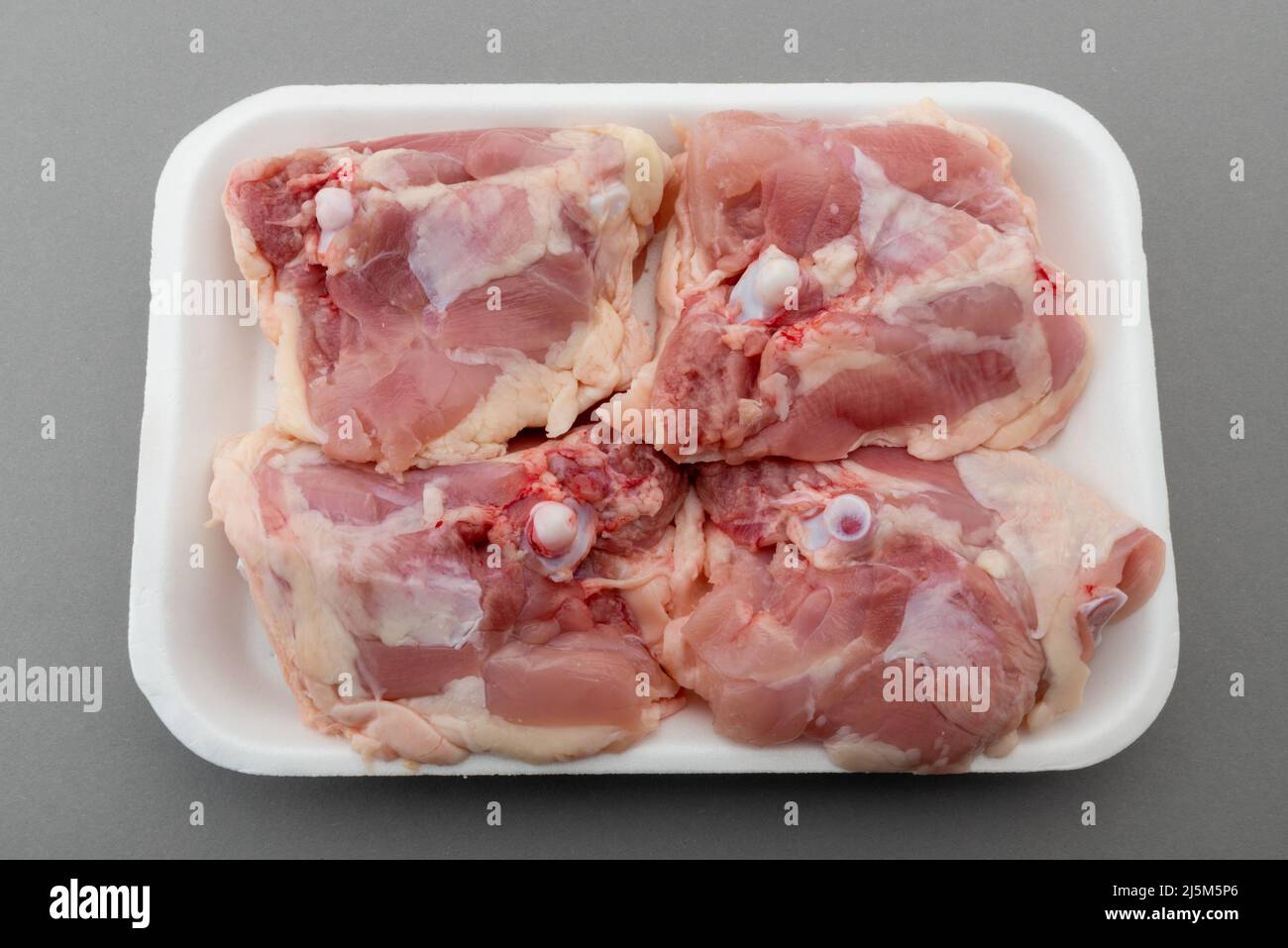 Chicken thighs in food plastic tray for sale in supermarket, isolated on gray background, clipping path Stock Photo